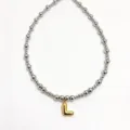 Close-up detail of silver stainless steel beaded necklace with gold bubble letter L pendant. - Letter L