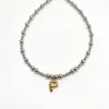 Close-up detail of stainless steel beaded choker necklace featuring gold bubble letter P. - Letter P