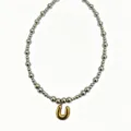 Close-up detail of silver bead chain necklace featuring a bold gold bubble letter U pendant. - Letter U