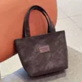Close up of a dark brown PU leather tote bag with double handles and a stylish front brand patch. - Coffee