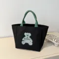 Black canvas tote bag with green handles and cute striped bear graphic for daily use. - Black