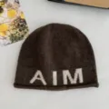 Braune Strickmütze für Damen mit weißer AIM-Buchstaben-Jaquard und gerollten Kanten. - Kaffeebraun