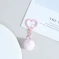 Detail des rosa Herz-Schlüsselanhängers mit flauschigem Pompon. Schickes Taschenaccessoire. - Rosa