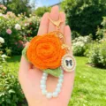 Handgestrickter orangefarbener Rosen-Schluesselanhänger mit Perlenband und eleganter Taschendetail. - Etikett-Stil 1