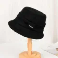 Close up of black wool-like bucket hat with elegant pleats and fashion label on wooden stand. - Adjustable / Black