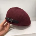 Close-up view of a wine red knitted beret hat featuring a stylish black leather strap buckle. - Burgundy