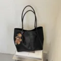 Detalle de bolso tote negro con doble asa, cuero texturado y lindo colgante de oso. - Con Colgante / Negro