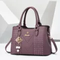 Purple leather shoulder bag detail, elegant metal logo accent, textured finish pendant. - Purple
