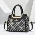 Detailed view of fashionable black diamond lattice shoulder bag with top handle and gold hardware. - Black