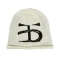 Nahaufnahme einer kuscheligen, cremeweißen Strickmütze mit auffälligem schwarzen Monogramm-Logo. - XL / Beige