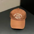 Close-up view of brown baseball cap featuring white embroidery text detail and soft crown. - Adjustable / Brown