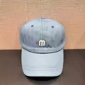 Close-up detail of the light blue baseball cap featuring a stylish white embroidered letter m. - Adjustable / Blue