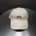 Detailopname van een beige honkbalpet met donkerbruin geborduurde letters aan de voorkant. - Verstelbaar / Beige