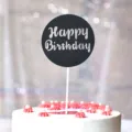 Nahaufnahme Detail des runden Happy Birthday Glitzer Kuchenaufsatzes auf dekoriertem Kuchen. - Glitzerndes Schwarz