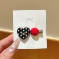Close-up detail of black polka dot heart and red ball hair clip on white display card. - Heart / 1 Piece / Black