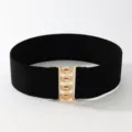 Detailed view of the wide elastic waist belt featuring a shiny gold metal buckle. - Black