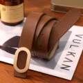 Close-up detail of stylish brown genuine leather women belt with elegant gold oval metal buckle. - Caramel color