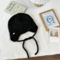 Detailansicht einer stylischen schwarzen Strickmütze mit Ohrenklappen und geflochtenen Bändern. - Einheitsgröße / Schwarz