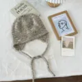 Gemütliche, mehrfarbig gesprenkelte Strickmütze mit Ohrenklappen und geflochtenen Bändern. - Einheitsgröße / Meliertes Grau