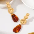 Gros plan de boucles d'oreilles longues élégantes avec disques dorés martelés et gouttes. - Style Goutte d'Eau en Résine Ambre (JMX-ER9829-C)