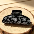 Close-up view of black acrylic hair claw clip with detailed white paisley and floral pattern. - Black