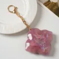 Detailed view of a stylish purple four-leaf clover keychain with gold chain and clasp. - Pink