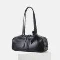 Detail view of the black leather bowling shoulder bag, showcasing fine grain texture and strap. - Black
