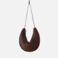 Close-up detail of the dark brown suede crescent shoulder bag hanging, showing soft texture. - Coffee