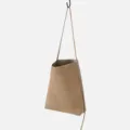 Detailed view of the minimalist frosted leather bucket shoulder bag hanging on display. - Apricot
