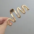 Vue détaillée d'une pince à cheveux élégante en métal doré ondulé pour des coiffures chics. - Style de Ligne Irrégulière / Or