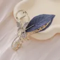 Vue détaillée d'une pince à cheveux dorée avec feuille brodée bleue et papillon en strass. - Pince Crabe Papillon Feuille Violette