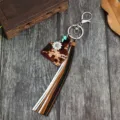 Primo piano di dettaglio del portachiavi con nappa in pelle bovina e ciondolo di girasole. - Lettera E