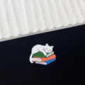Detail shot of a creative cat enamel pin featuring a cute white cat sleeping on a colorful stack of books. - White Cat Sleeping on Books Style (R213)