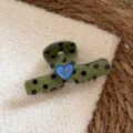 Detailed shot of a green polka dot hair claw clip with a cute blue heart charm on soft fabric. - Green Polka Dot / Green