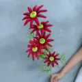 Nahaufnahme Detail des roten künstlichen Blumenastes mit lebendigen Blüten und grünen Blättern. - Sonnenblume