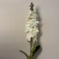 Primo piano di uno stelo di fiore bianco artificiale con petali delicati e foglie verdi. - Speronella Bianco