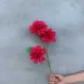 Nahaufnahme von lebendigen roten künstlichen Dahlienblüten mit grünen Blättern für Dekor. - Dahlien
