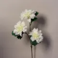 Primo piano dettagliato di un ramo di dahlie bianche artificiali con tre fiori e foglie. - Dalia