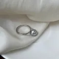 Detalle en primer plano del anillo ajustable plateado con perla gris en tela blanca - Abierto Ajustable / Gris