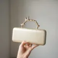 Gold evening clutch detail showing unique metal branch handle and premium leather texture. - Champagne
