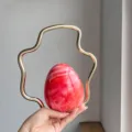 Detailed view of the unique red gradient egg-shaped evening bag with a chic wavy gold handle. - Orange Red