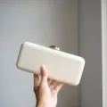 White evening clutch bag detail showing premium leather texture and elegant gold clasp design. - White