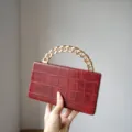 Detailed view of the red crocodile texture hard clutch bag with a chunky gold chain handle. - Burgundy