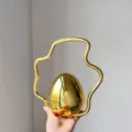Detail shot of a gold metallic egg-shaped evening bag with an irregular curved handle. - Gold
