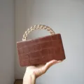 Close-up of brown crocodile pattern box handbag featuring a metallic gold chain handle. - Tan