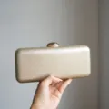 Gold metallic clutch bag detail shot, sleek leather texture evening purse with metal clasp. - Champagne