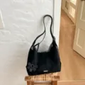 Vista detallada de un elegante bolso de hombro negro con colgante floral en taburete. - Negro