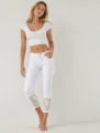 Detailed view of women's white cropped jeans featuring delicate lace cuffs and slim fit. - S / Bottoms / White