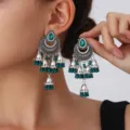 Detailed shot of vintage silver ethnic jhumka earrings with green stones and beaded tassels. - Green