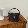 Vista detallada de bolso cubo de cuero marrón oscuro con cierre metálico y costuras claras. - Con Colgante / Café